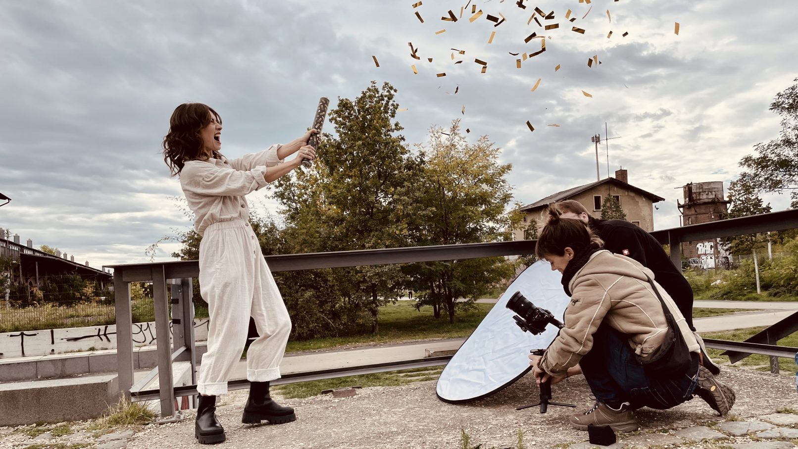 Eine Frau feuert eine Konfetti-Kanone ab. Rechts neben ihr hockt eine Frau an einer Kamera und dahinter ein Mann mit einem Reflektor.